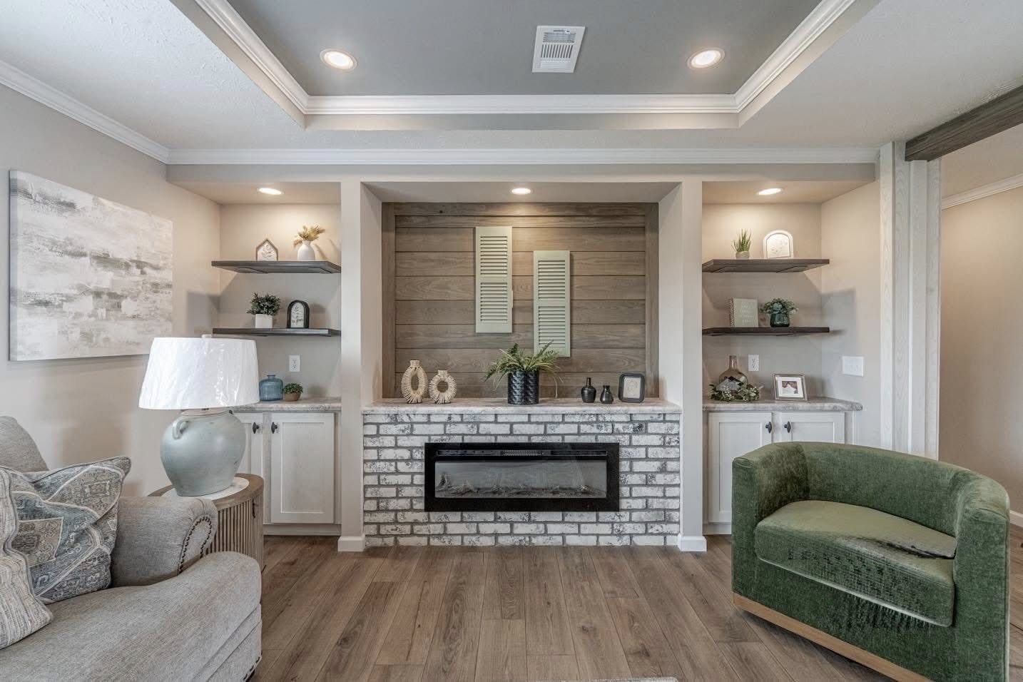 A cozy living room featuring a brick fireplace with decorative shutters and plants. Shelves hold small decor items. Soft lighting creates a warm ambiance.