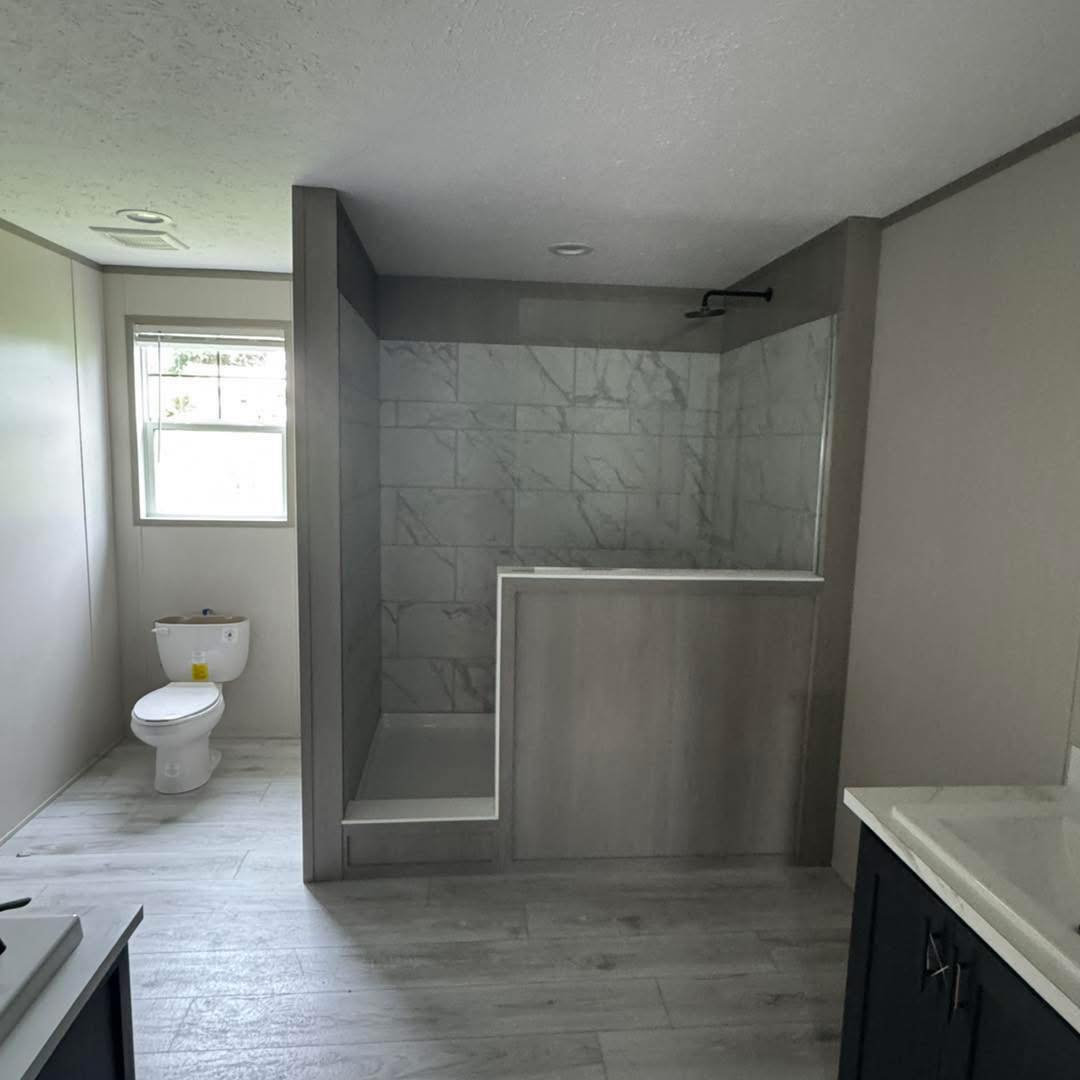 Modern bathroom with a walk-in marble-tiled shower, adjacent toilet, and natural light from a window. The ambiance is minimalistic and clean.