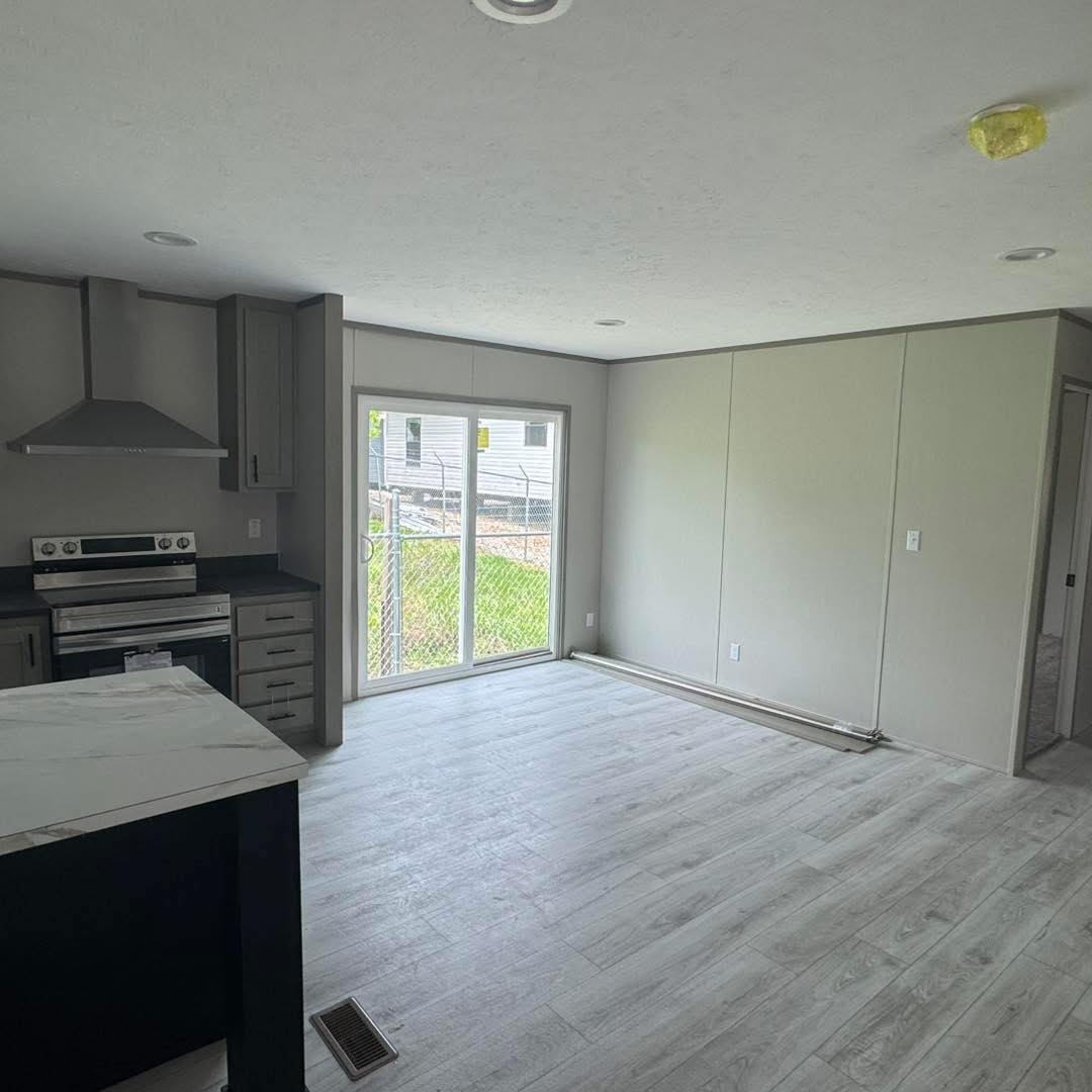 Bright, modern interior with light wood flooring, a stainless steel kitchen with black countertops, sliding glass door, and neutral walls.