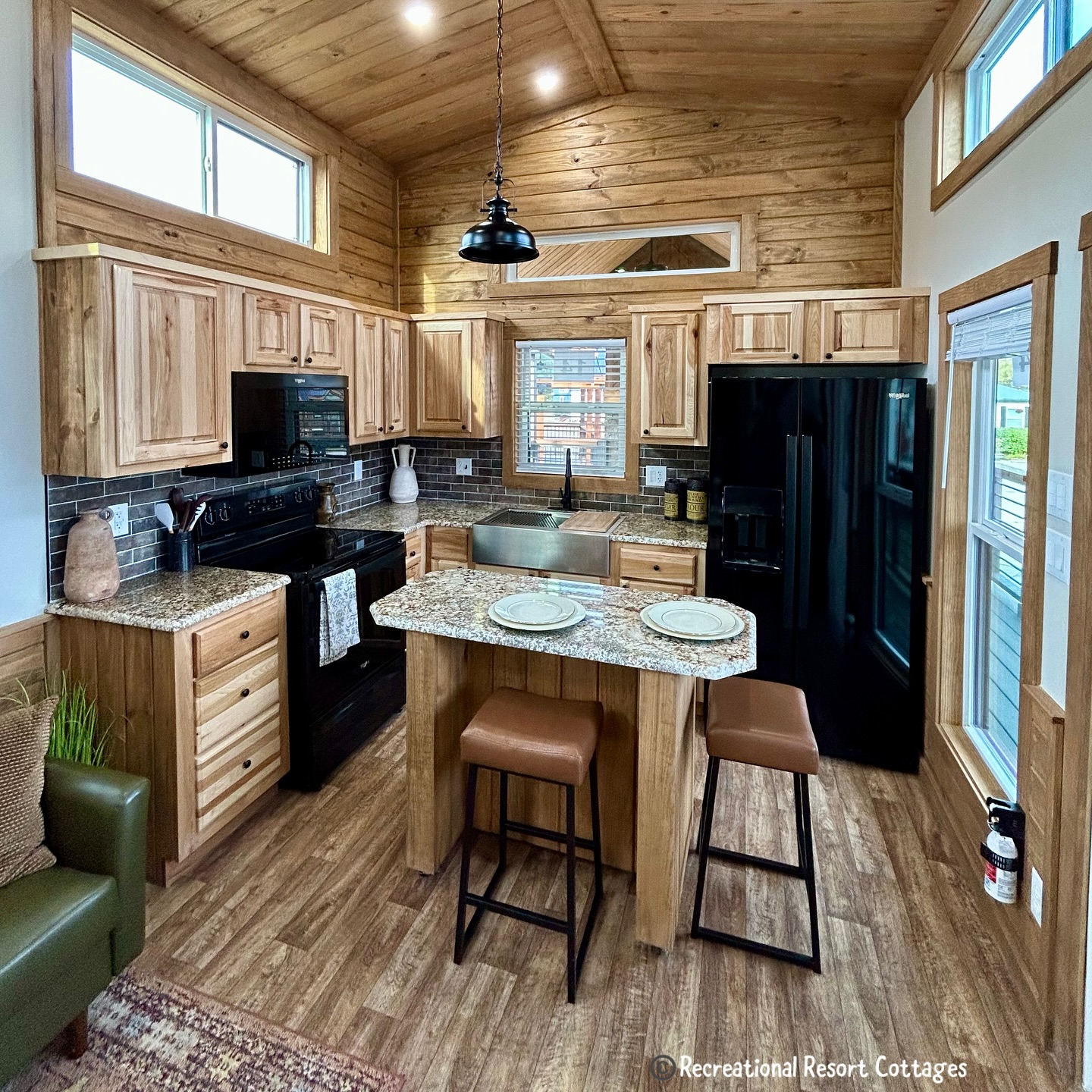 Cozy kitchen with wooden cabinets, granite countertops, and stainless steel sink. Features black appliances, an island with seating, and rustic decor.