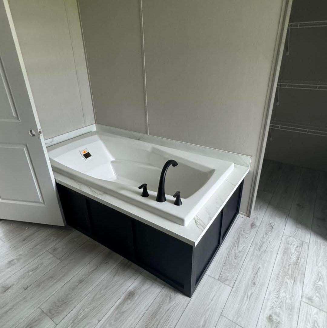 Modern bathroom with a white rectangular bathtub featuring black fixtures. Light wood flooring adds a clean and minimalist touch.