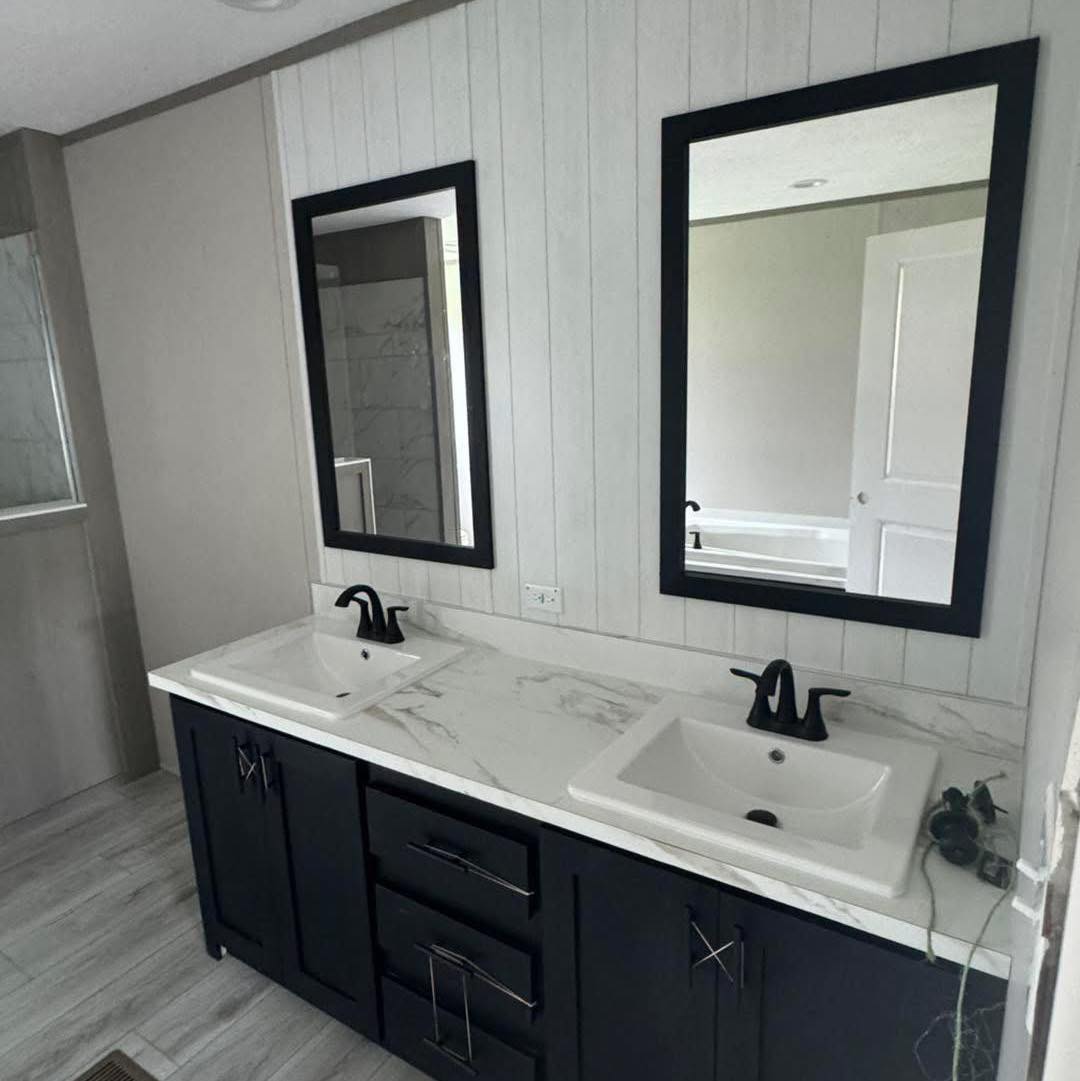 Modern bathroom with dual sinks on a marble countertop, black cabinetry, and two black-framed mirrors. The space is sleek and minimalistic.