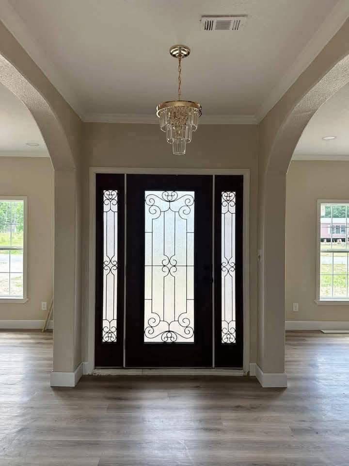 Elegant entryway with ornate glass doors framed by tall windows, adorned by a classic chandelier. The mood is welcoming and sophisticated.