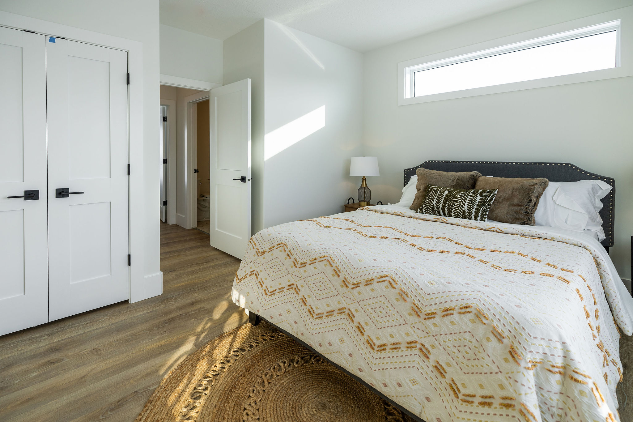 Cozy bedroom with a large bed featuring a patterned quilt and decorative pillows, a bedside lamp, wood floor, and neutral walls for a serene feel.