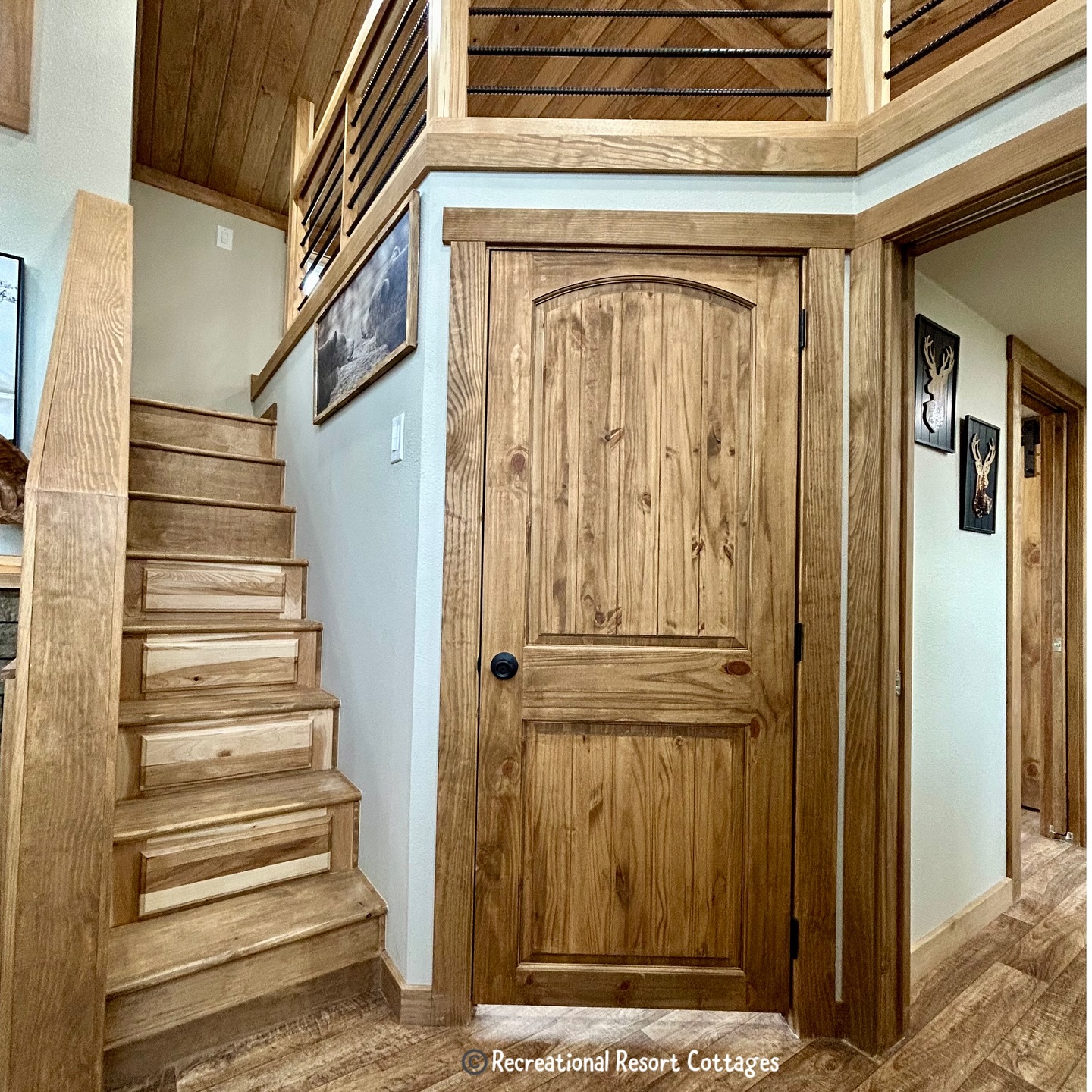 Wooden interior with a rustic staircase leading to an upper level. A solid wood door is next to the stairs. Warm tones create a cozy atmosphere.