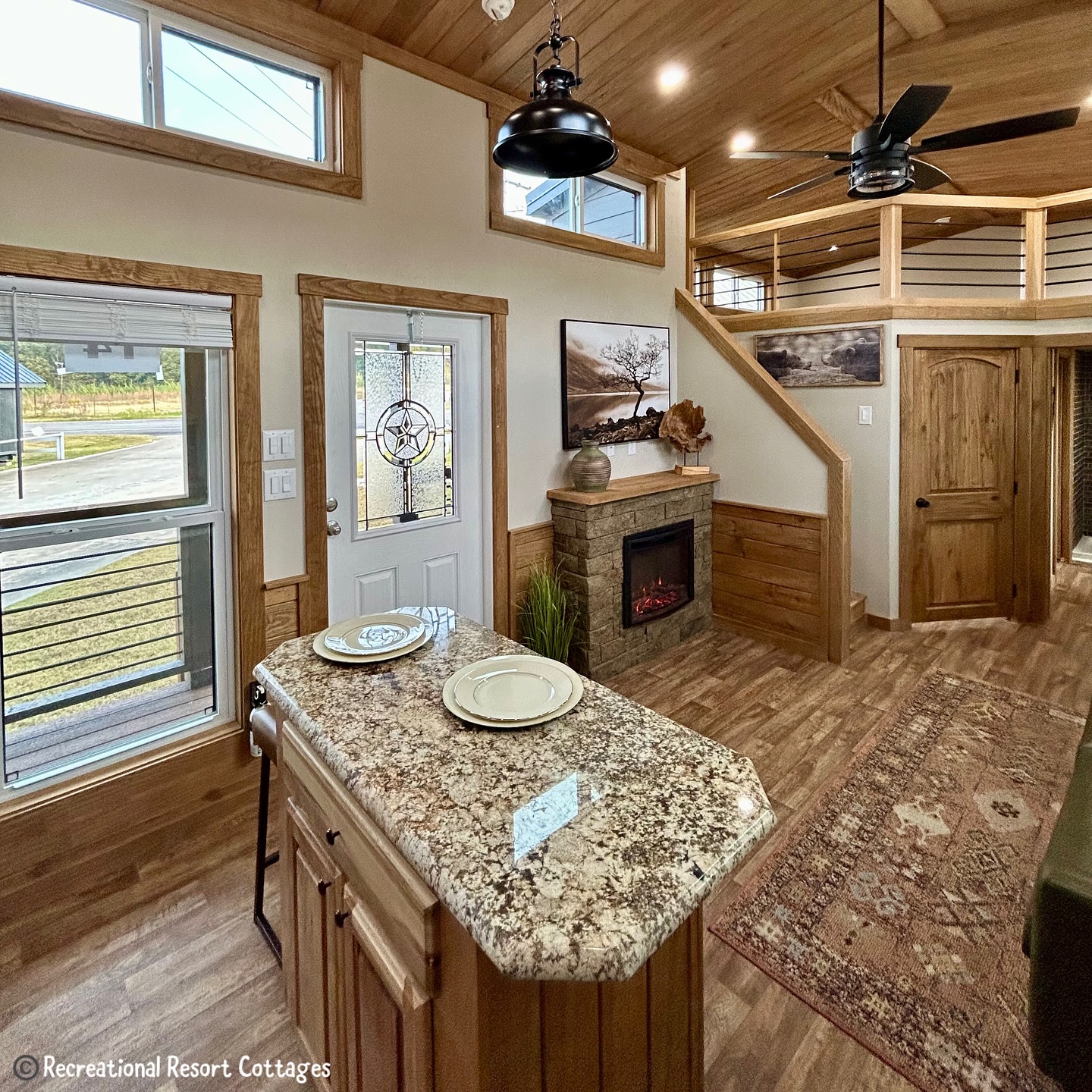 Cozy living space with a rustic theme. Features a kitchen island with granite countertop, a decorative fireplace, and wood accents. Warm, inviting ambiance.