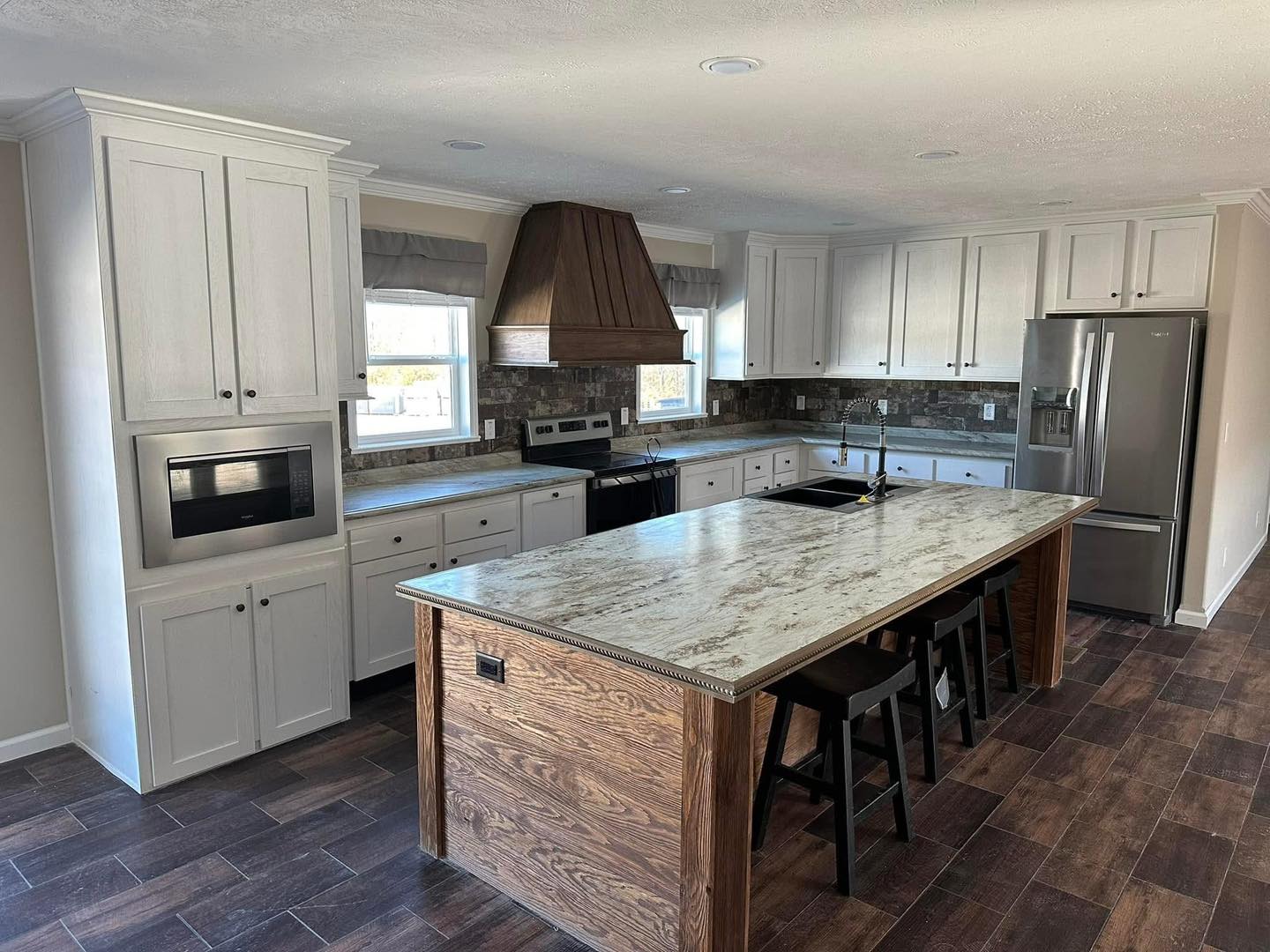 Modern kitchen with a large marble island, wooden accents, and white cabinetry. Stainless steel appliances and tiled backsplash create a clean, inviting atmosphere.