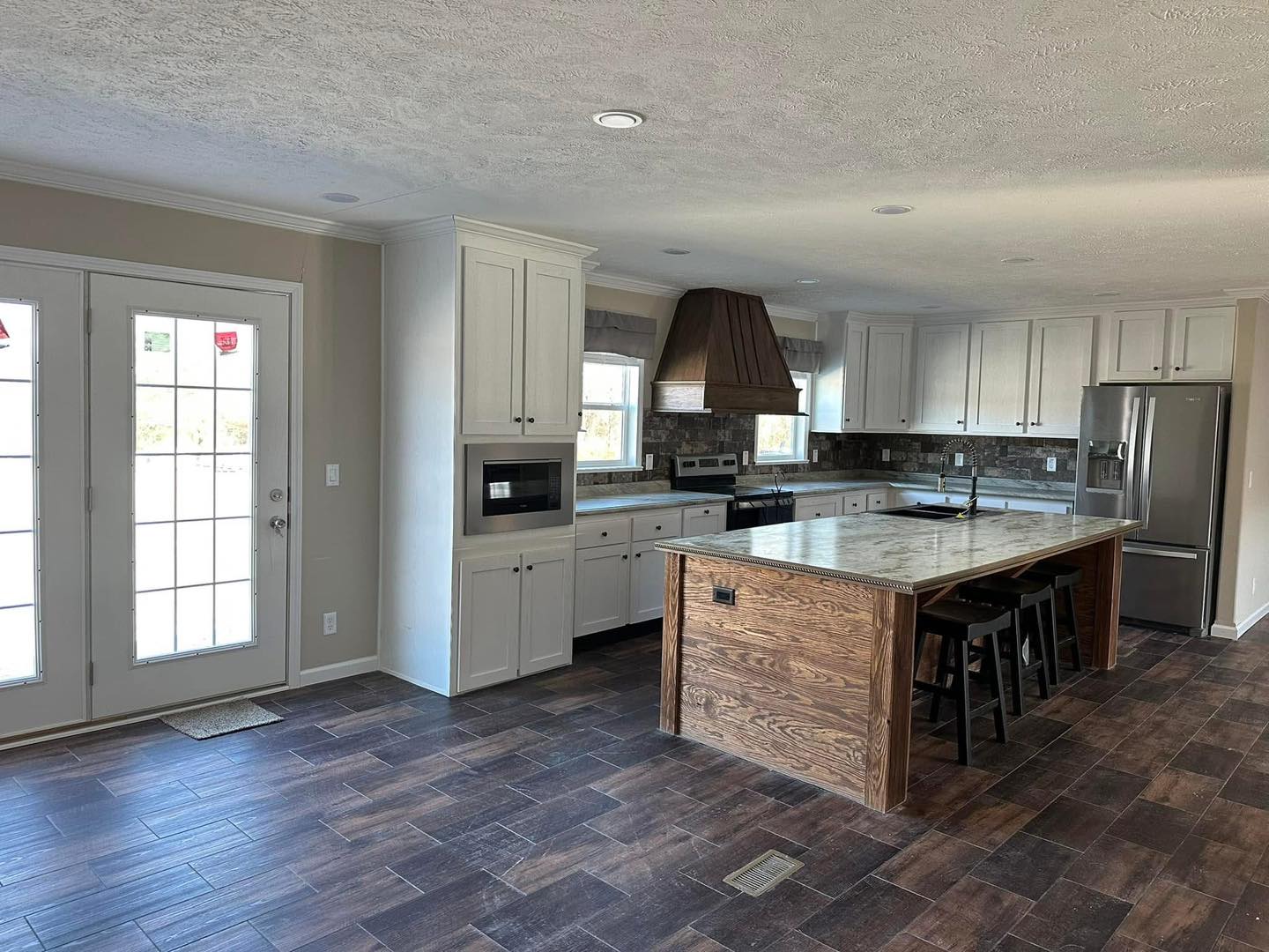 Spacious kitchen with white cabinets and a large wooden island. Stainless steel appliances, tile backsplash, and a dark wood floor enhance its modern look. French doors provide natural light.