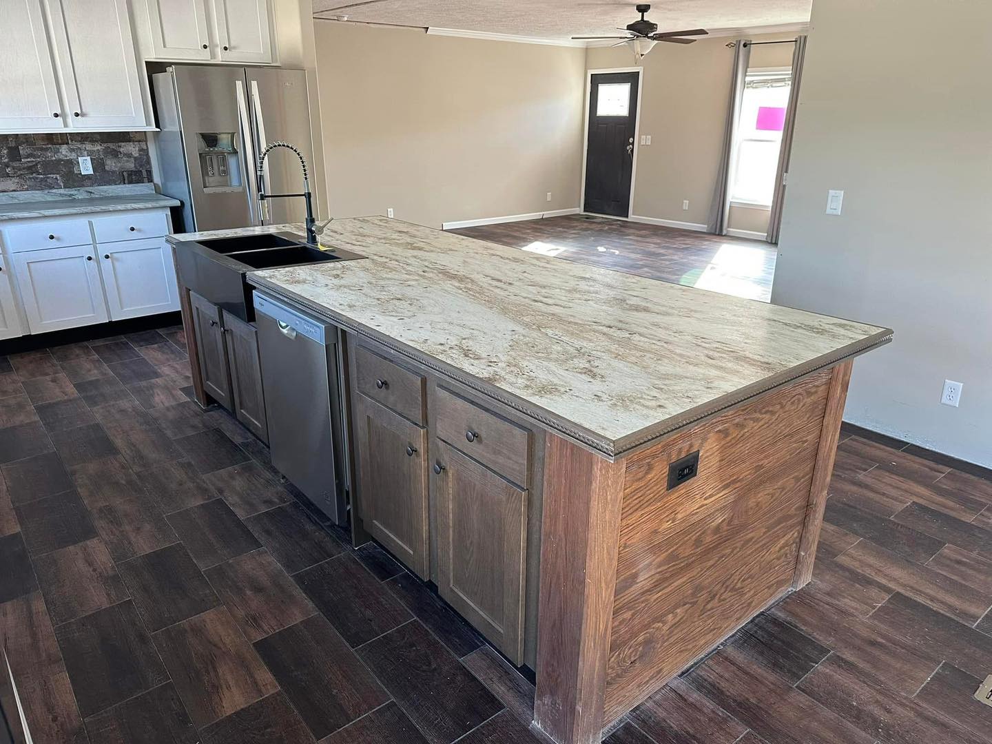 A spacious kitchen with a large wooden island featuring a light granite countertop. It has dark wood flooring, stainless steel appliances, and white cabinets.