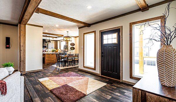 Modern living area with wooden beams, dark wood floors, and a geometric rug. The space connects to a dining area with hanging lights, exuding warmth.