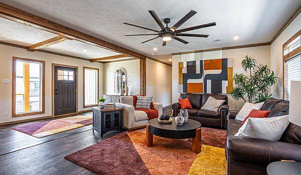 Bright, modern living room with large geometric artwork, dark leather sofas, colorful cushions, a ceiling fan, and warm-toned rugs, creating a cozy atmosphere.