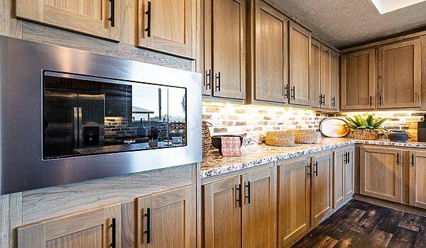 Warm kitchen scene with wooden cabinets, a stainless steel microwave, granite countertops, and under-cabinet lighting. Cozy and inviting ambiance.