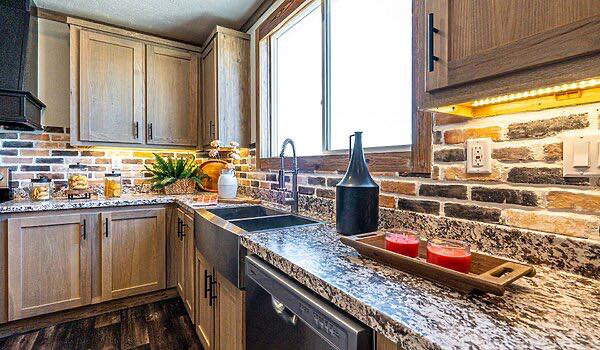 Modern kitchen with wooden cabinets, brick backsplash, and granite countertops. Includes a sink, wine bottle, and candles, creating a cozy ambiance.