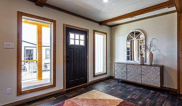 Bright entryway with dark wooden flooring, large black door, two tall windows, geometric-patterned console, decorative mirror, and vases. Cozy and modern.
