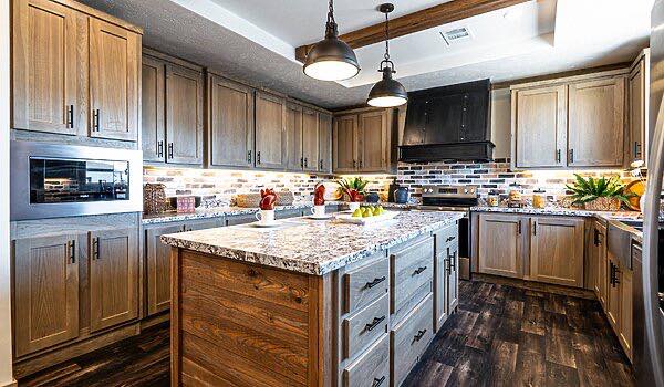 Spacious kitchen with wooden cabinets, marble countertops, and a central island. Brick backsplash, pendant lighting, and potted plants add warmth.