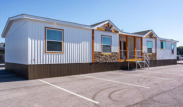 A white modular building with stone accents, two front steps, and four windows, standing in an empty parking lot on a sunny day, conveying a modern style.