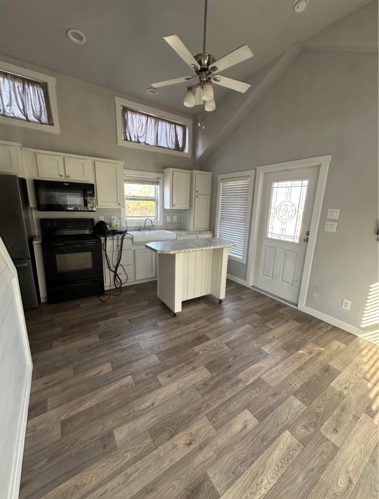 A modern kitchen with vaulted ceilings, featuring white cabinets, a black oven, a central island, and wood flooring. It feels open and bright.