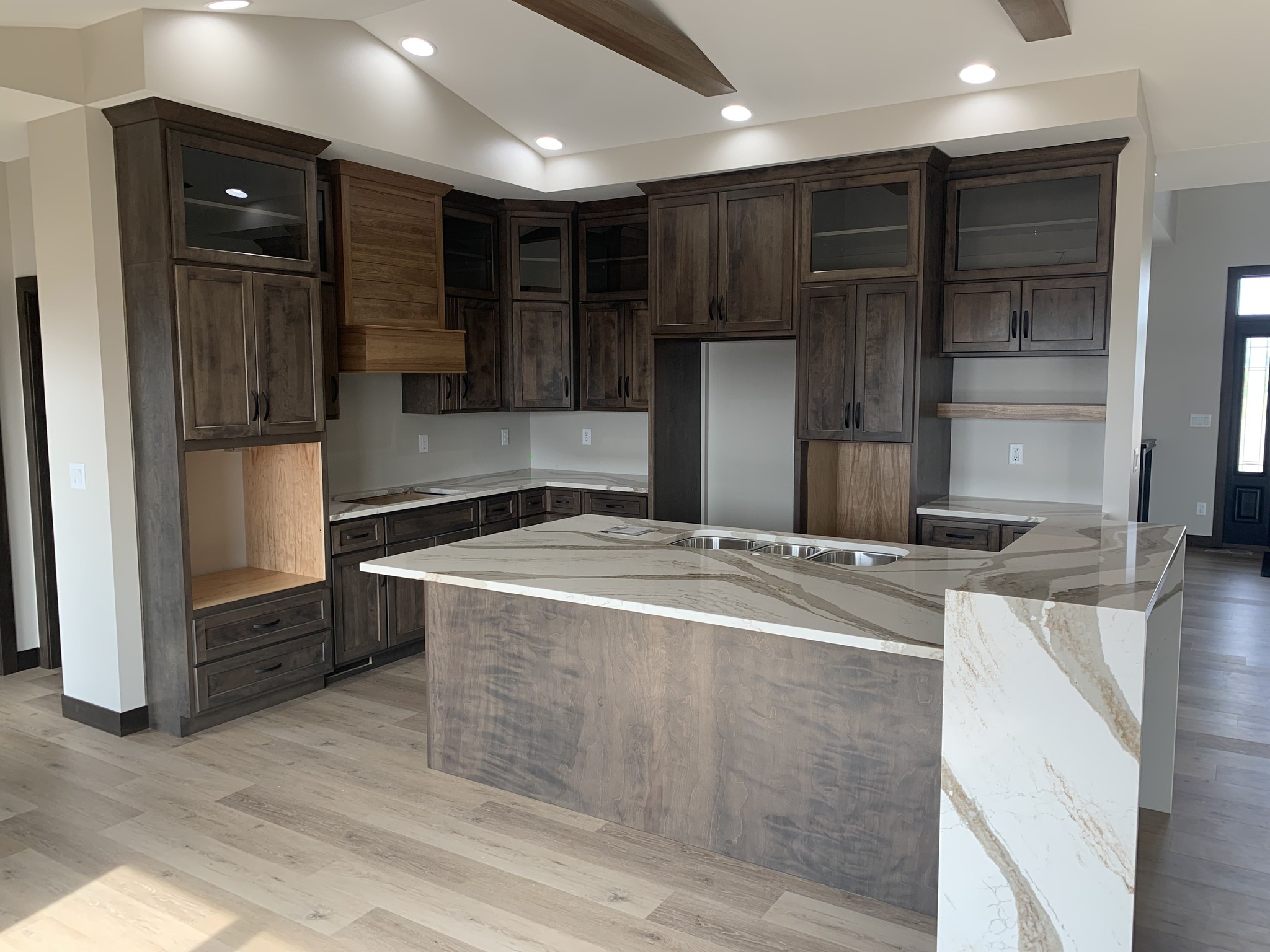 Spacious kitchen with dark wooden cabinets, a marble-patterned island, stainless steel sink, and light wood floors, conveys a modern and inviting tone.