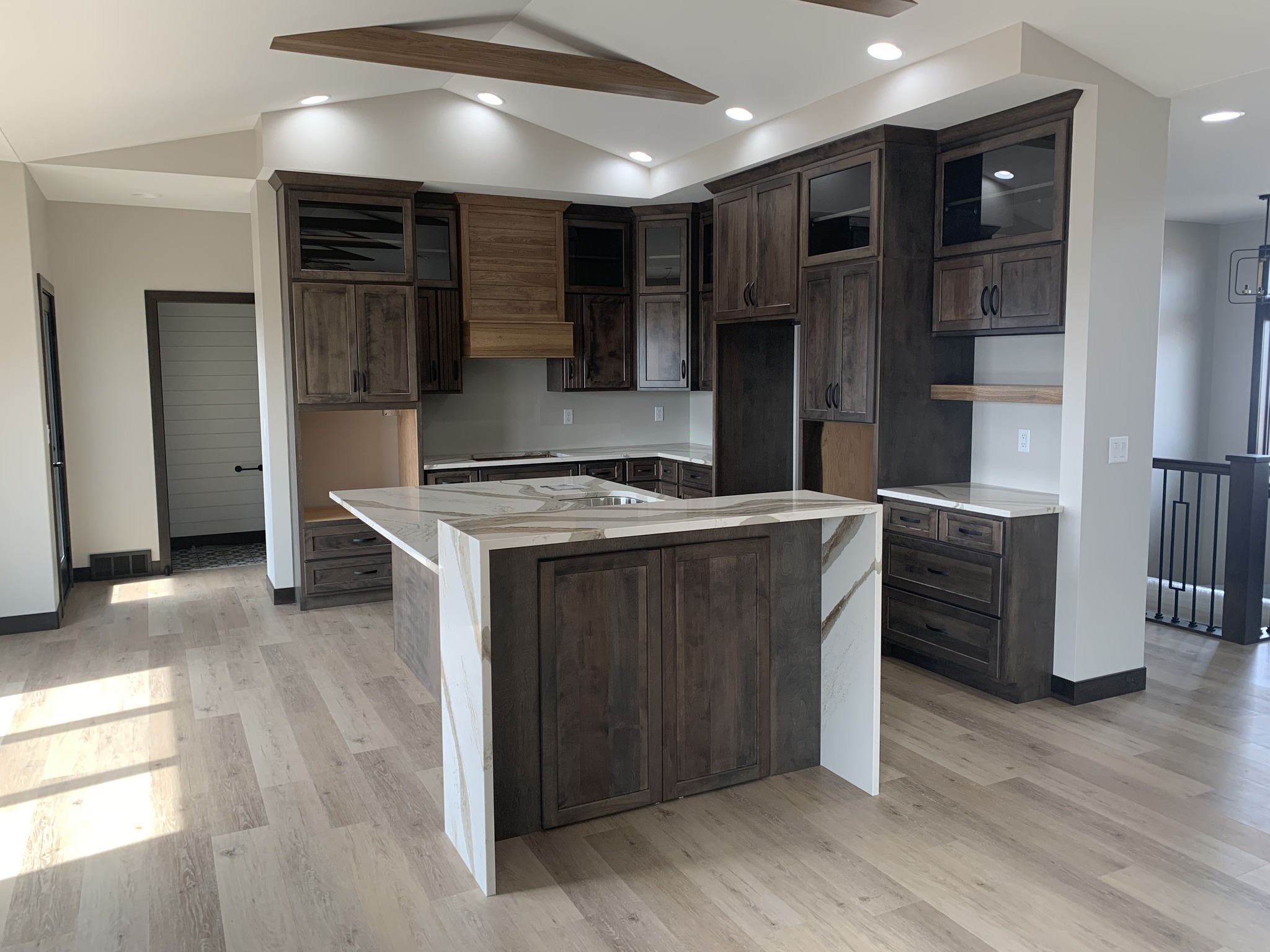 Kitchen with dark wooden cabinets, marble island, and light wood flooring. Recessed lighting and ceiling fan create a modern and inviting atmosphere.