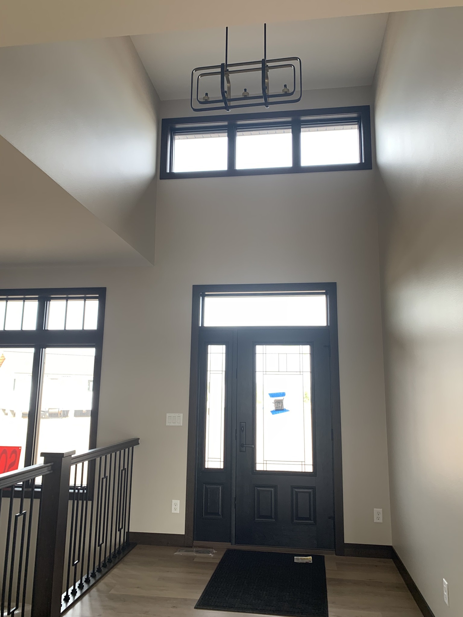 Spacious entryway with tall ceilings and a modern chandelier. Features a large black door with glass panels and a sidelight, plus an upper window.