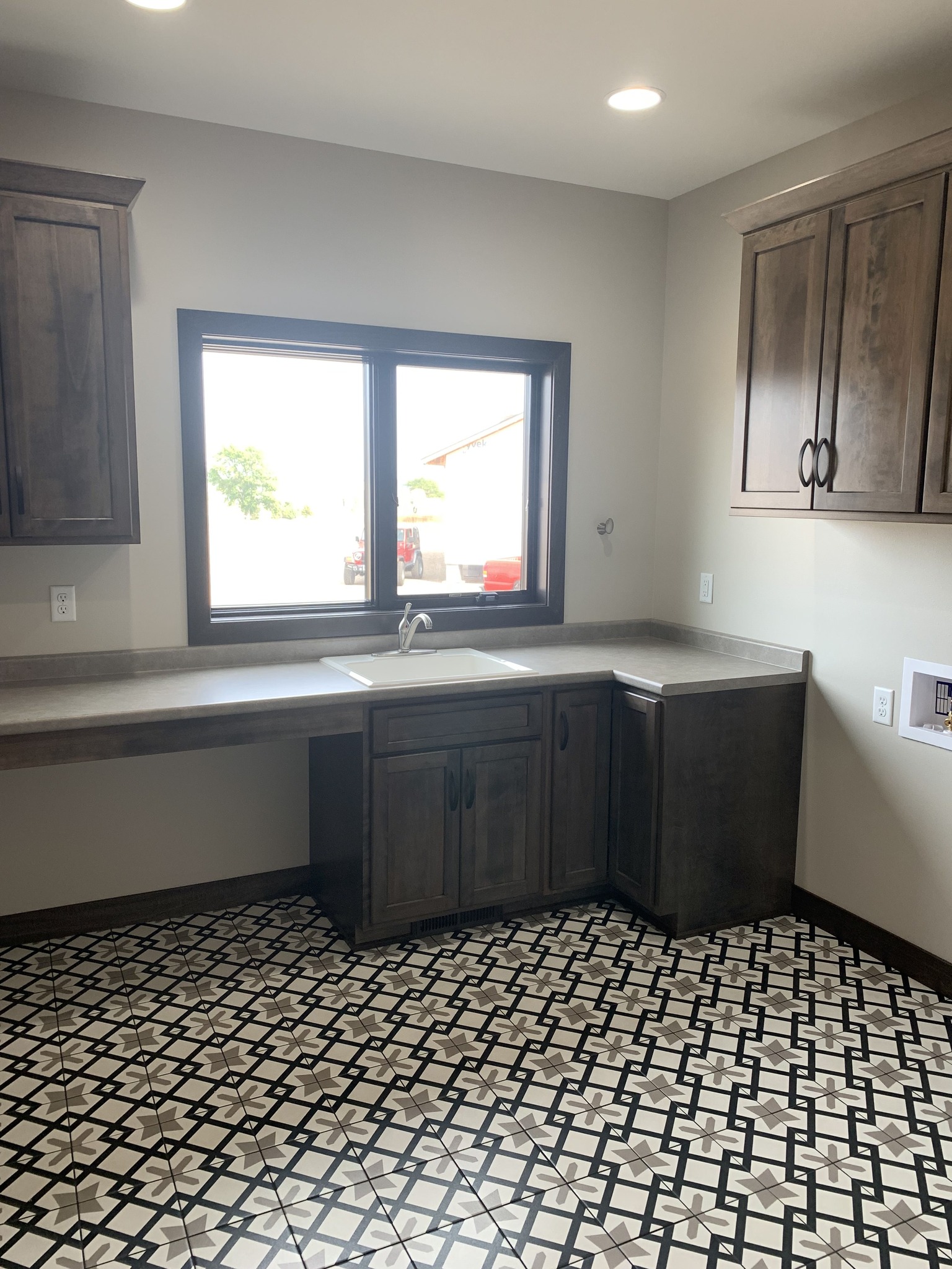 A kitchen with dark wood cabinets, a dual sink under a window, and patterned black-and-white floor tiles. The space feels bright and modern.