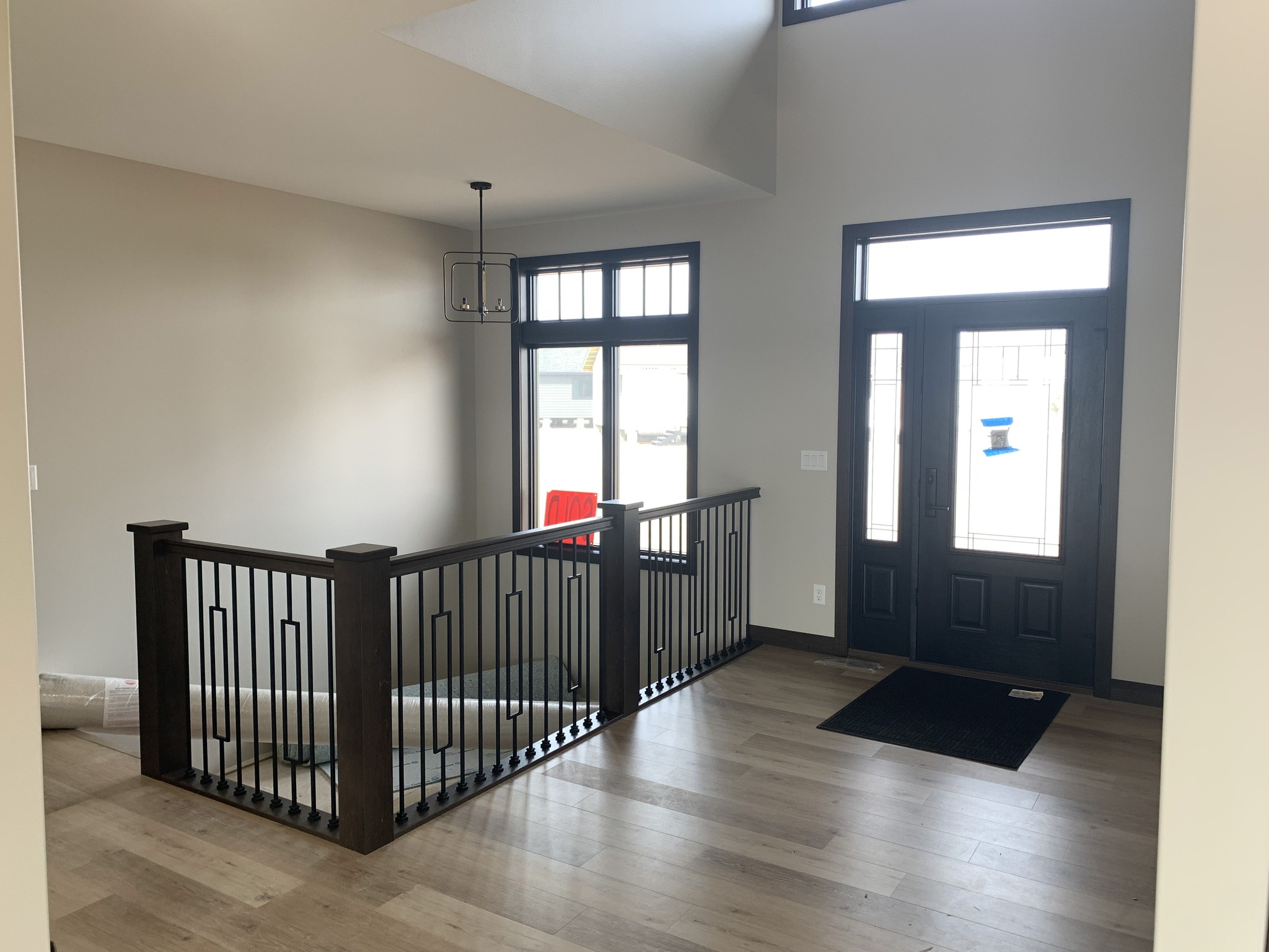 Bright entryway featuring a black-framed glass door, sleek wooden stairs with wrought-iron railing, light wood flooring, and a modern pendant light.