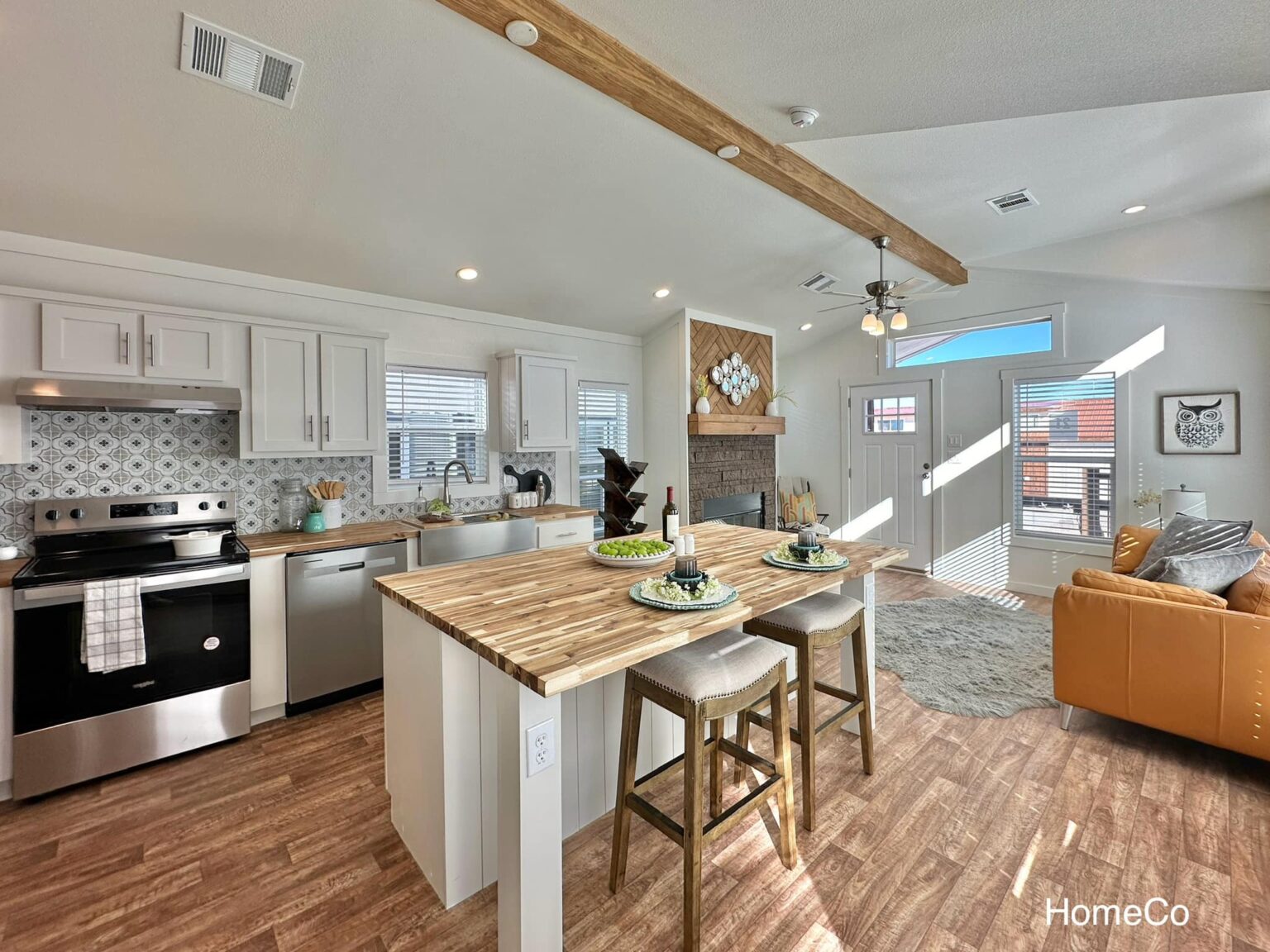 Modern kitchen and living room with wood accents. Features a large island with stools, cozy seating area, and ample natural light. Inviting and stylish.