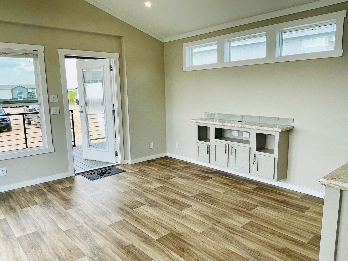 Bright, modern room with light wood flooring, beige walls, and a small built-in cabinet. Open glass door and windows enhance airy ambiance.