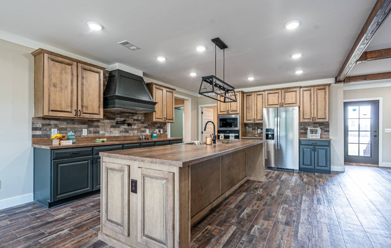 Spacious kitchen with rustic wood cabinets, large island, and stainless steel appliances. The brick backsplash and wood floor add warmth and charm.
