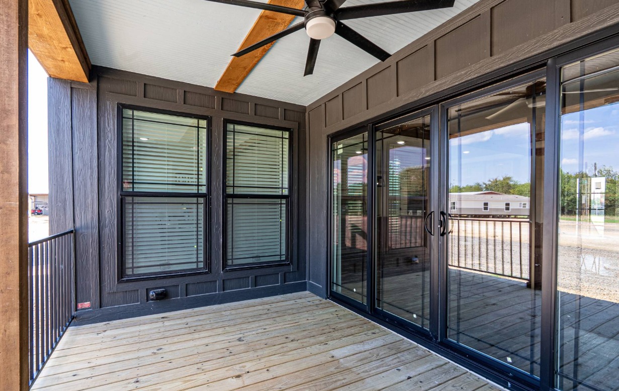 Enclosed patio with wooden deck, black-framed windows, sliding glass doors, and a ceiling fan. Sunlight streams in, creating a bright, inviting space.