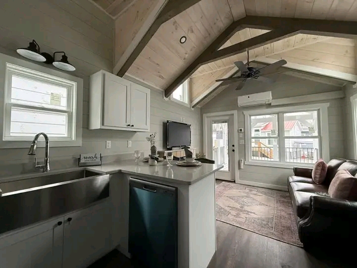 Bright, cozy living area with a vaulted ceiling and exposed beams. Features a kitchen island, leather sofa, and large windows offering ample natural light.