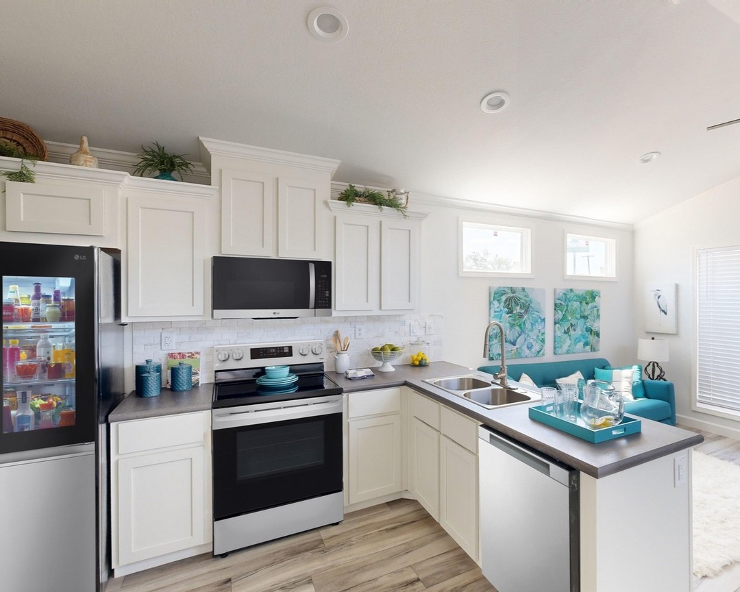 Modern kitchen with white cabinets, stainless steel appliances, and a visible stocked fridge. Bright and airy with teal accents and artwork.