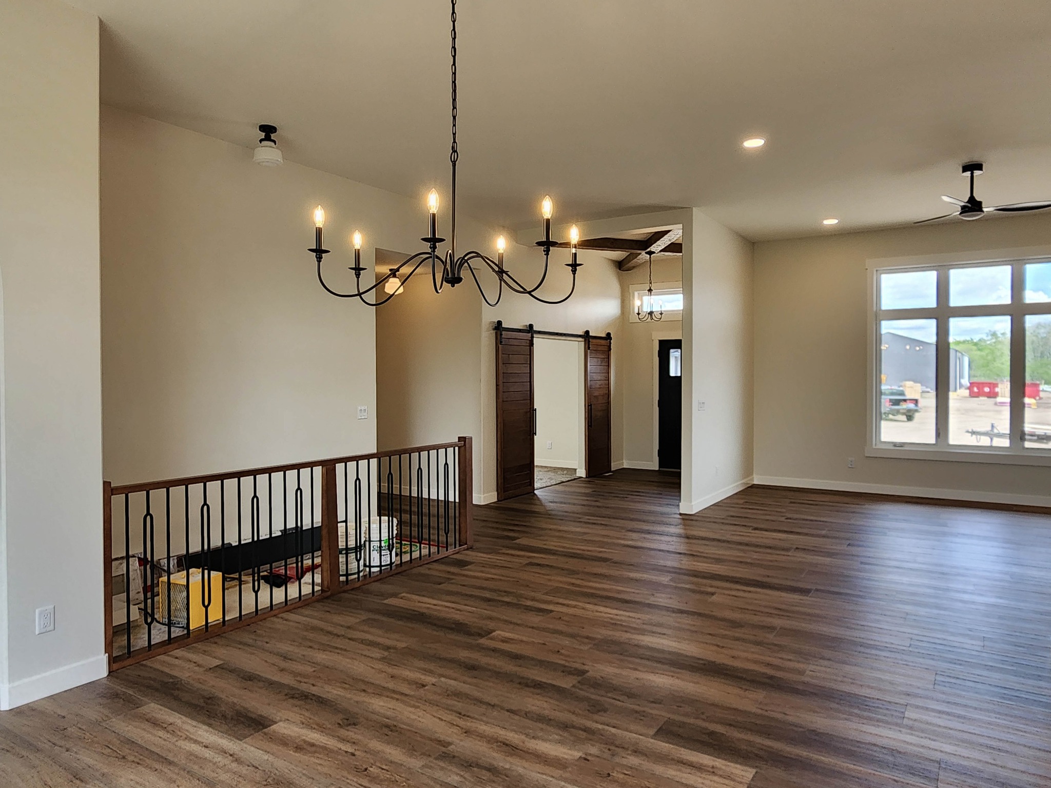 Spacious living area with wood flooring, elegant chandelier, large window, and barn-style sliding doors. Bright and airy ambiance with modern decor.
