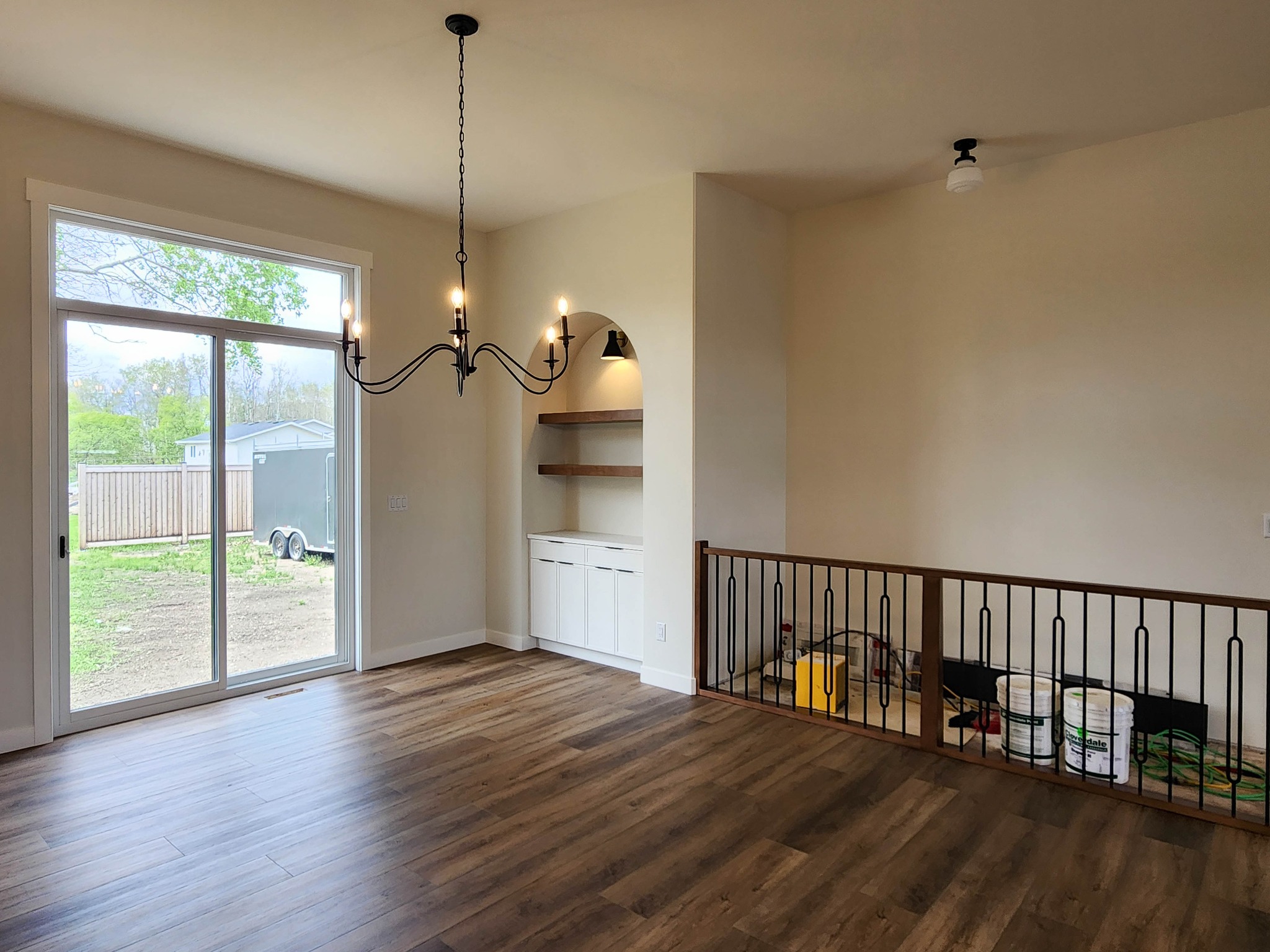 Spacious room with hardwood floors, a modern chandelier, and large sliding glass door leading outside. Built-in shelving and white cabinets under warm lighting.