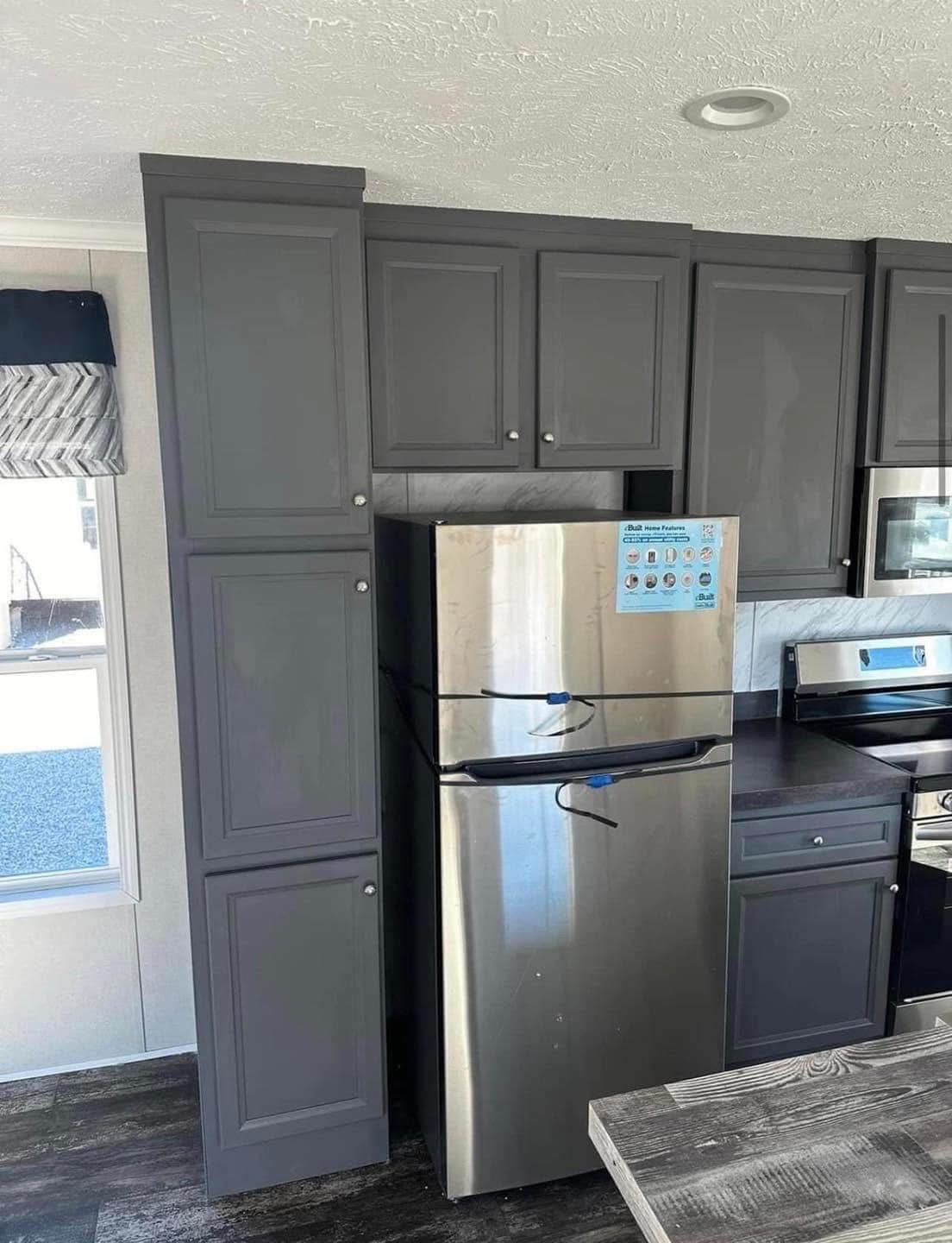 Modern kitchen with sleek gray cabinets and a stainless steel refrigerator, complemented by dark countertops. The space is bright and contemporary.