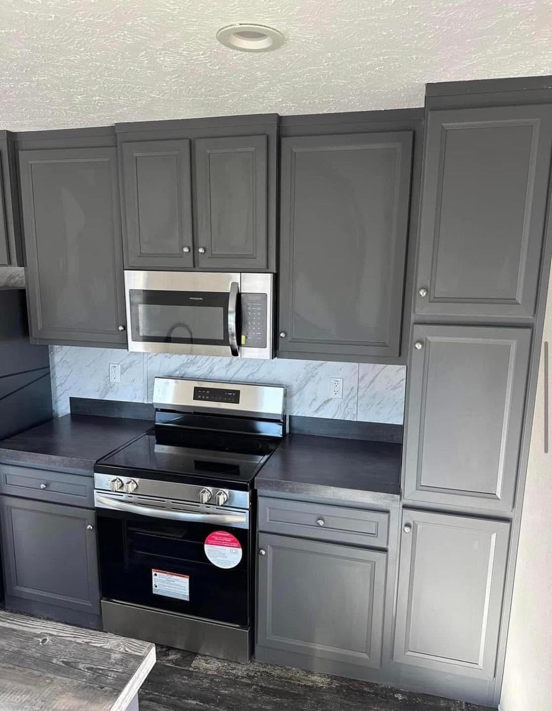 Modern kitchen with sleek gray cabinets and black countertops. A stainless steel microwave and stove are centered, against a white marble backsplash.