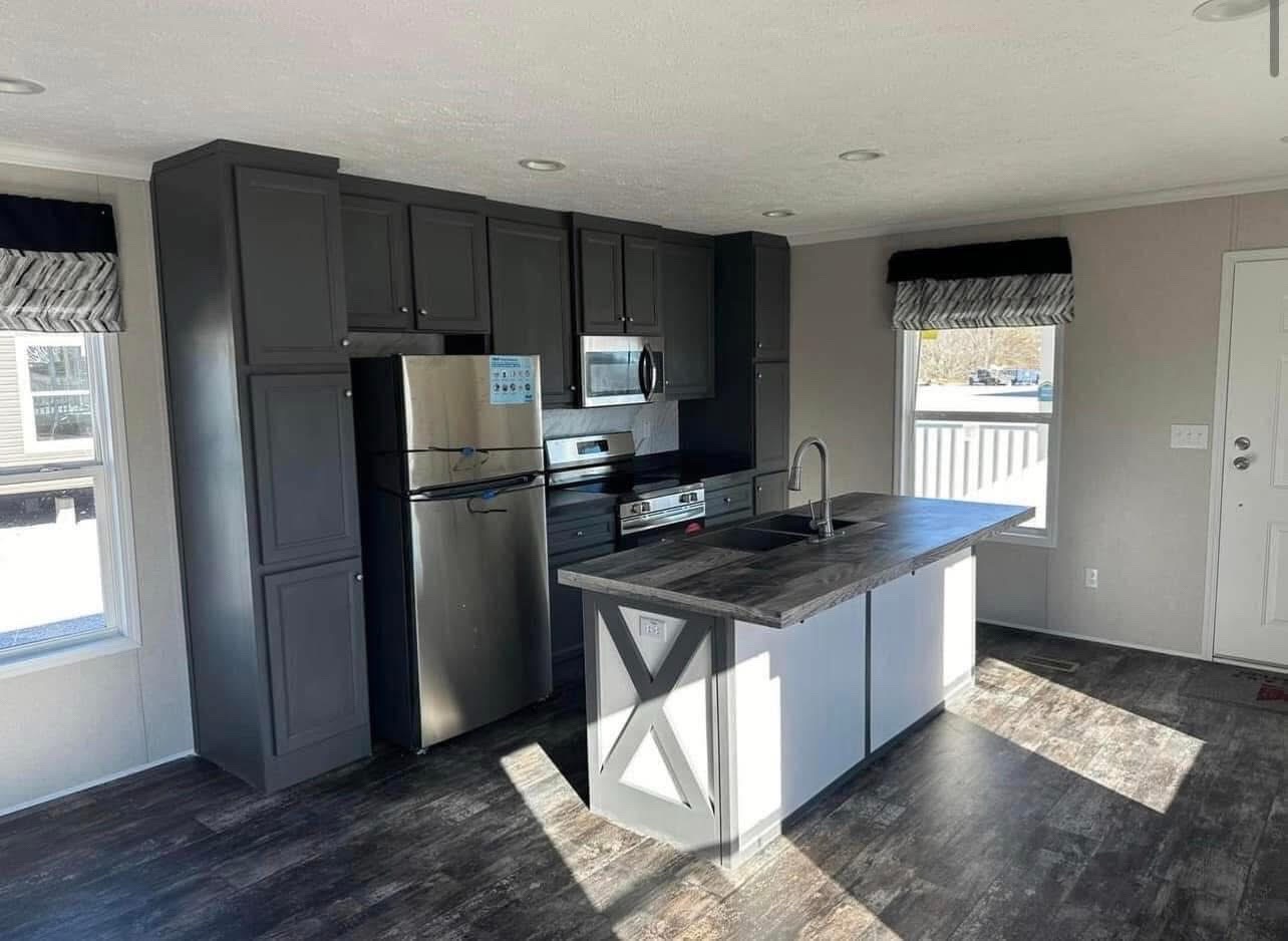 Modern kitchen with dark gray cabinets and stainless steel appliances. Large island with a sink, dark countertops, and bright natural light. Cozy and inviting.