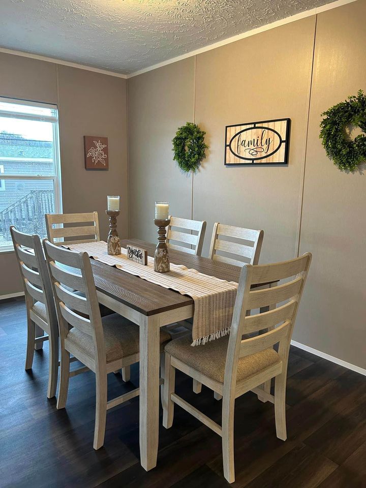 Cozy dining room with a wooden table set for six. Two candles and a "Thankful" sign adorn the table. Walls feature wreaths and a "Family" sign.