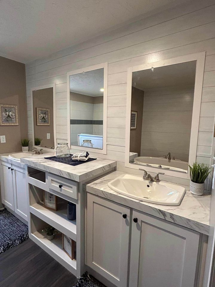 Bright bathroom with two white cabinets and sinks, marble countertops, and large mirrors. Decor includes potted plants and artwork, creating a serene atmosphere.