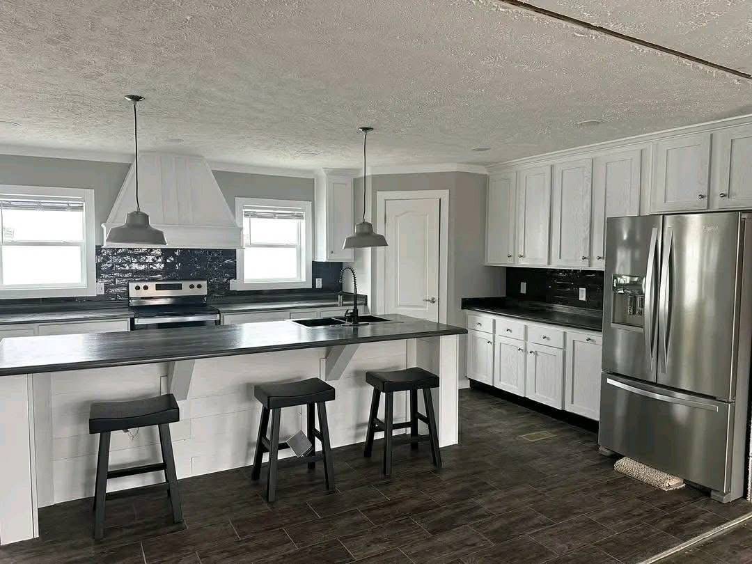 Modern kitchen with dark wood floors, sleek white cabinets, and gray countertops. Features a large island with three stools and stainless steel appliances.