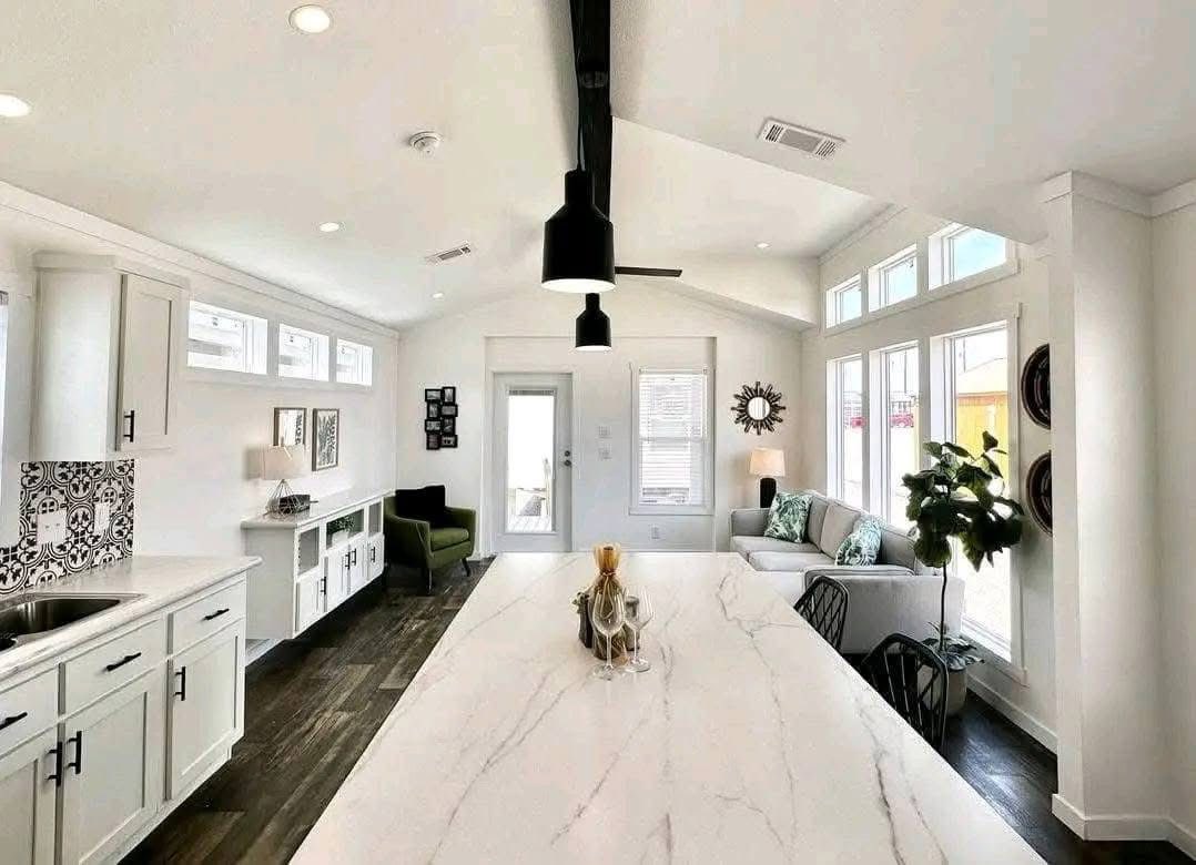Bright, modern open-concept living area with a marble kitchen island, black pendant light, and a cozy seating area. Large windows and sleek decor add elegance.