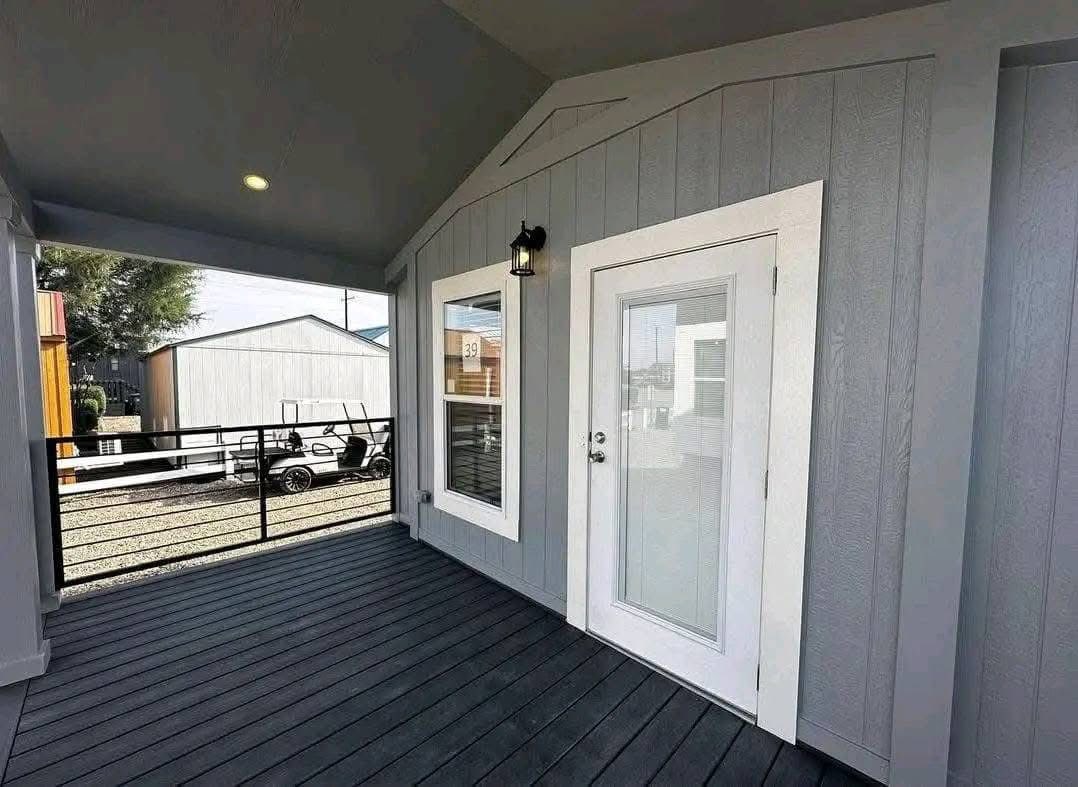 Covered patio with gray walls, a white-trimmed door, and a window. Natural light and a black railing offer an inviting, serene feel.