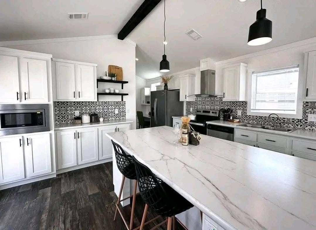 Modern kitchen with white cabinets, patterned black-and-white backsplash, and a large marble island with black pendant lights above. Cozy and stylish.
