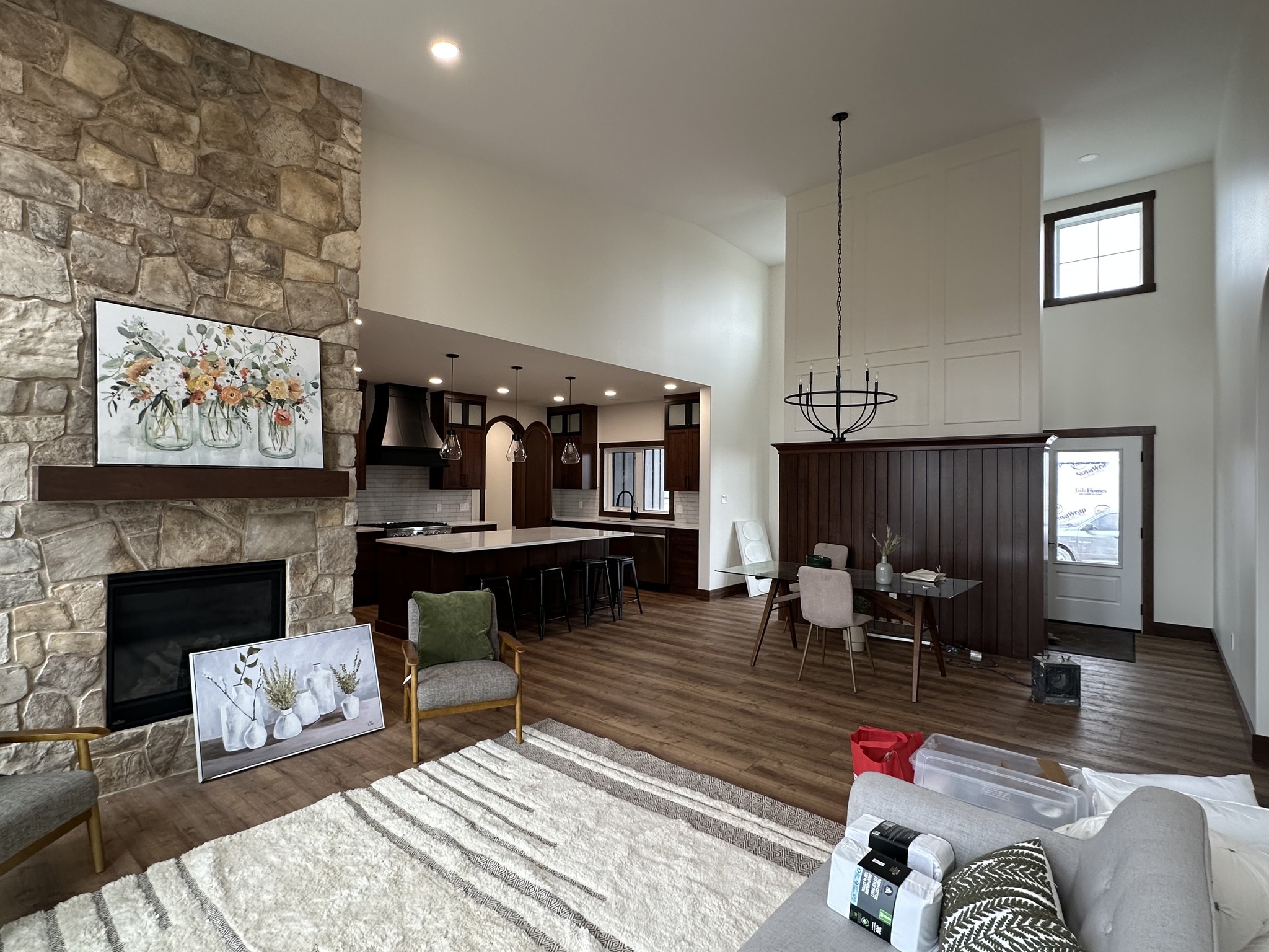 Spacious living area with a stone fireplace, floral artwork, and a view into a modern kitchen. Dining table with chairs and warm wood accents. Cozy and inviting.