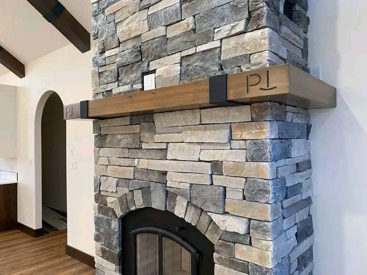 Rustic stone fireplace with a wooden mantle engraved with "PL" in a bright, cozy room. The arched doorway adds a classic touch.