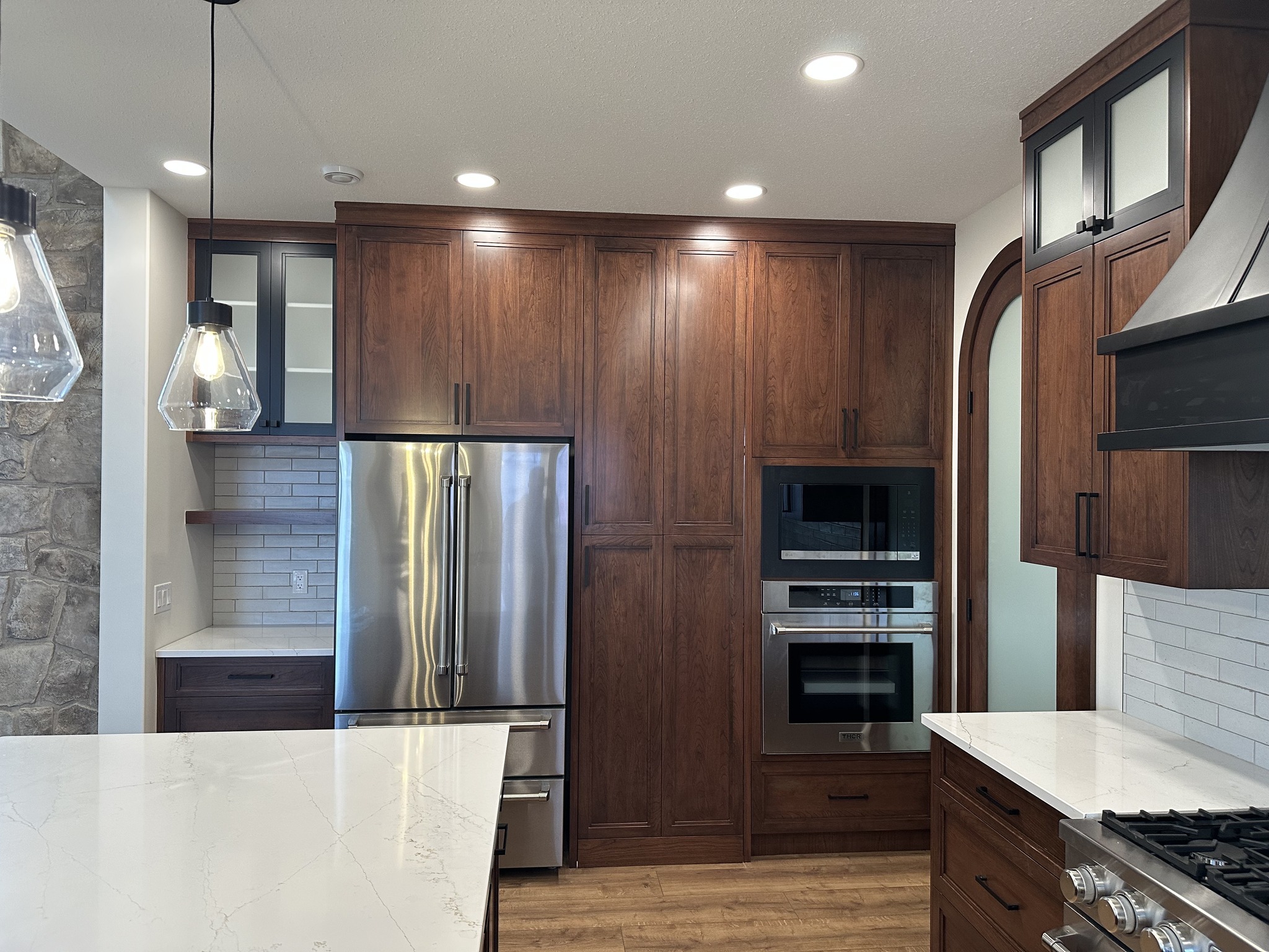 Modern kitchen with dark wood cabinets, stainless steel appliances, and white quartz countertops. Pendant lights and stone accents add elegance.