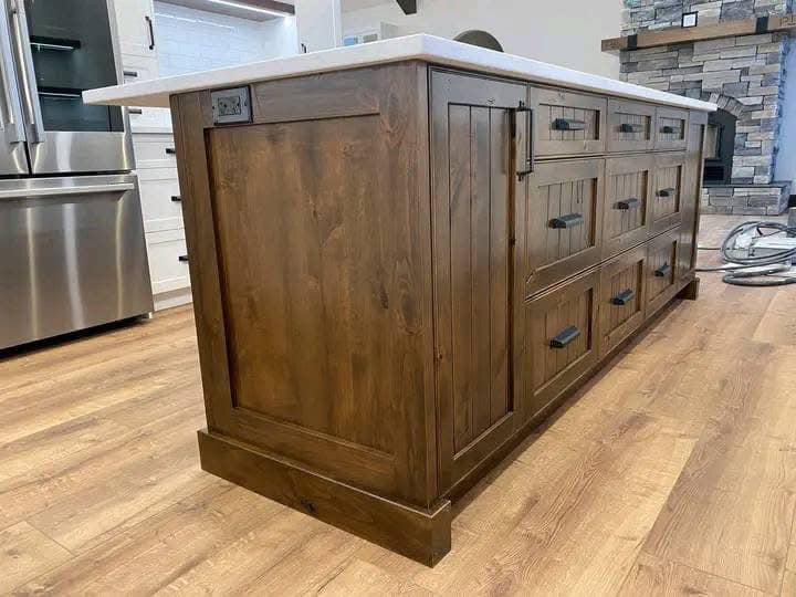 Rustic wooden kitchen island with dark handles sits on hardwood flooring. The countertop is white, and to the side is a stainless steel oven.
