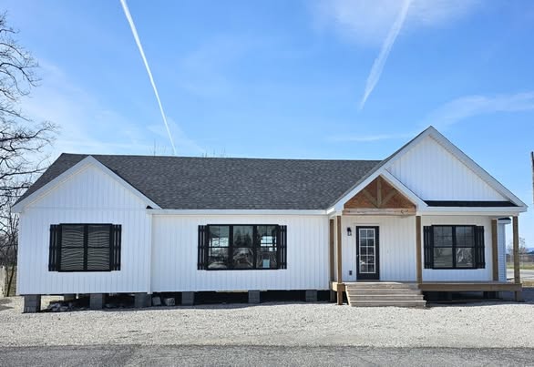 Single-story white house with black shutters, a dark roof, and small front porch. The setting is a clear day with a blue sky and visible contrails.