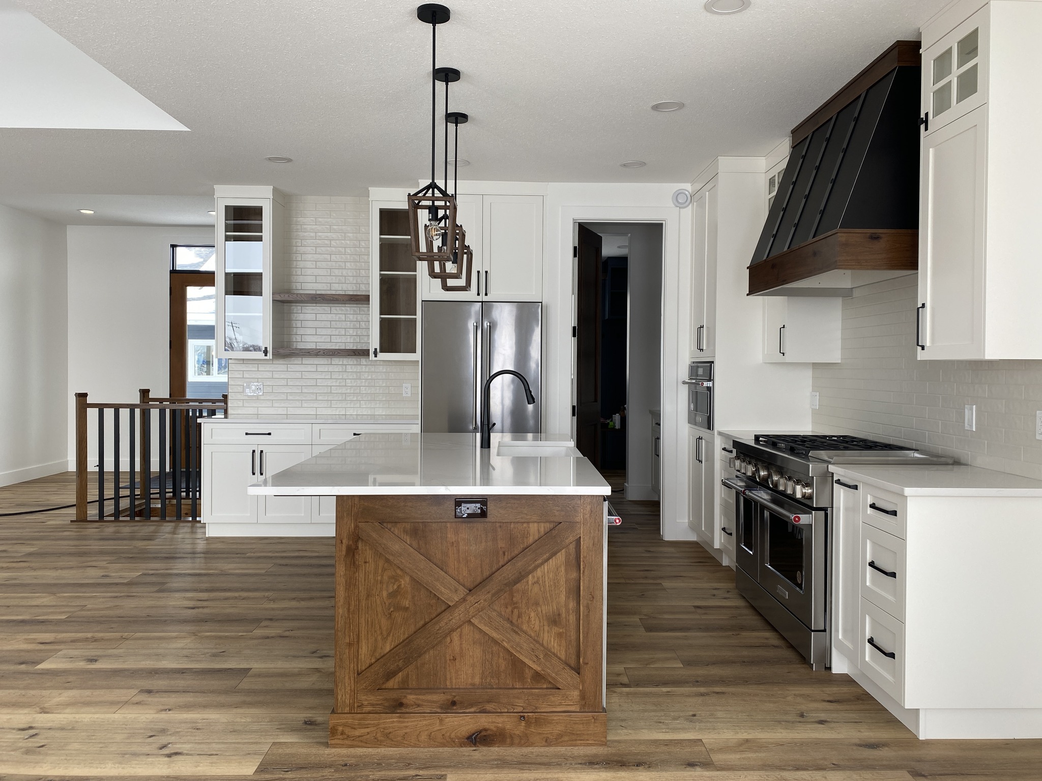 Spacious modern kitchen with a white island featuring a wooden base, hanging light fixtures, stainless steel appliances, and light wood flooring.