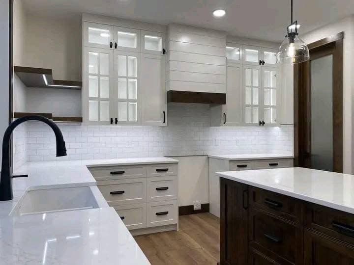 Modern kitchen with white cabinets, black handles, and glass-paneled doors. Features dark wood accents, white countertops, and a pendant light.